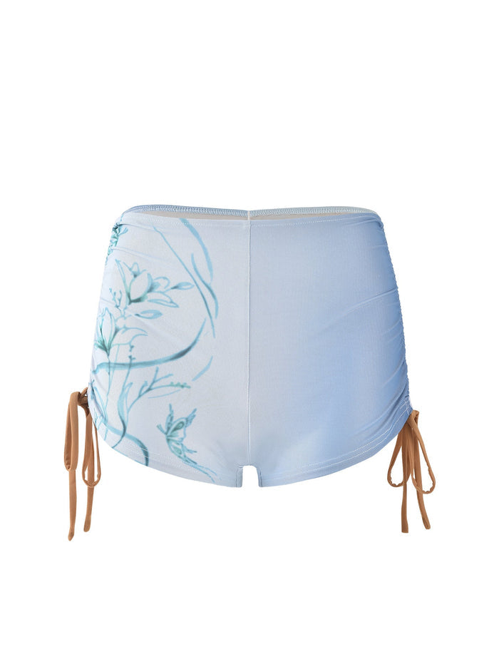 A pair of high-waisted, light blue Elvera Shorts by TIGERMIST featuring a delicate floral design on the back. The shorts have adjustable tan drawstrings on both sides, allowing for a ruched effect. The material appears smooth and stretchy, suited for casual or beachwear.