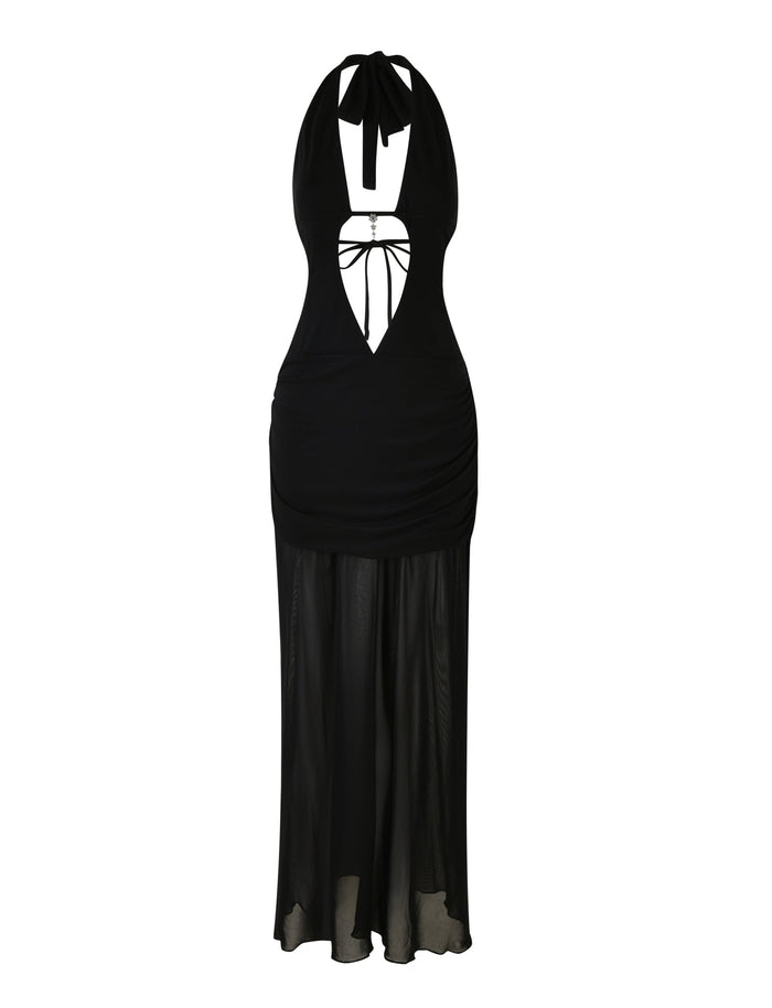 The ESHA MAXI DRESS - BLACK by TIGERMIST is a halter-neck dress with a deep V-cut neckline, featuring cut-out details and a tied bow at the chest. The dress has a fitted bodice that transitions into a flowy, semi-sheer maxi-length skirt reaching the ankles.