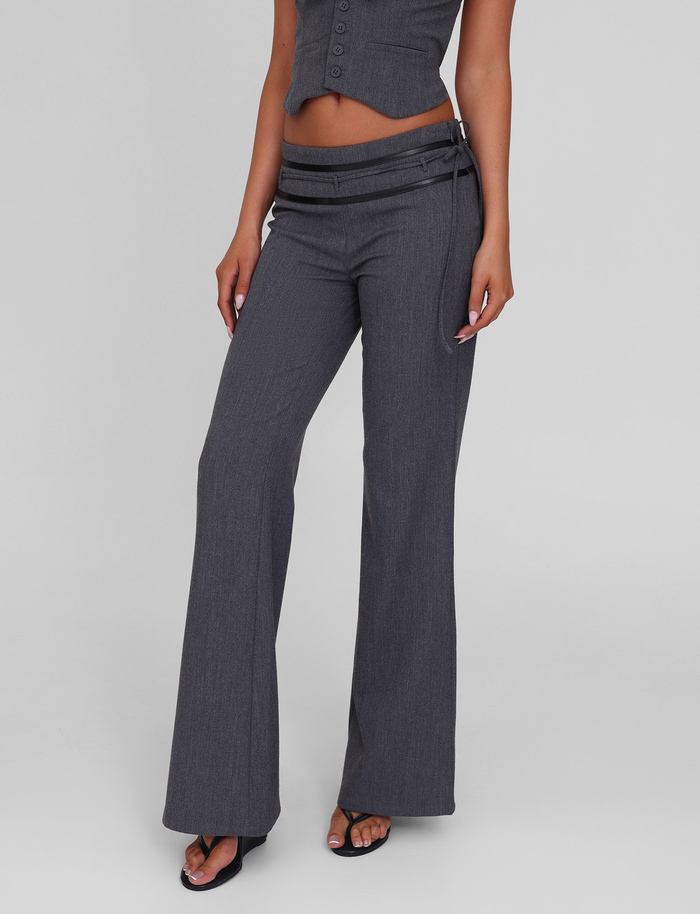 Someone wears the TIGERMIST FEDRA PANT - GREY, featuring a tailored fit, flared legs, and double waistband detail. They're paired with a matching fitted top and black heeled sandals against a plain light background.