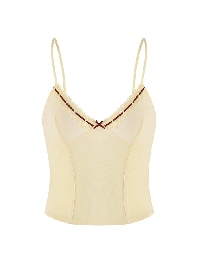 The FENNEL TOP - YELLOW from TIGERMIST is a pale yellow cami top with thin straps, showcasing a delicate lace trim along the neckline and accented with a small burgundy bow at the center. The smooth fabric offers a simple yet elegant design.