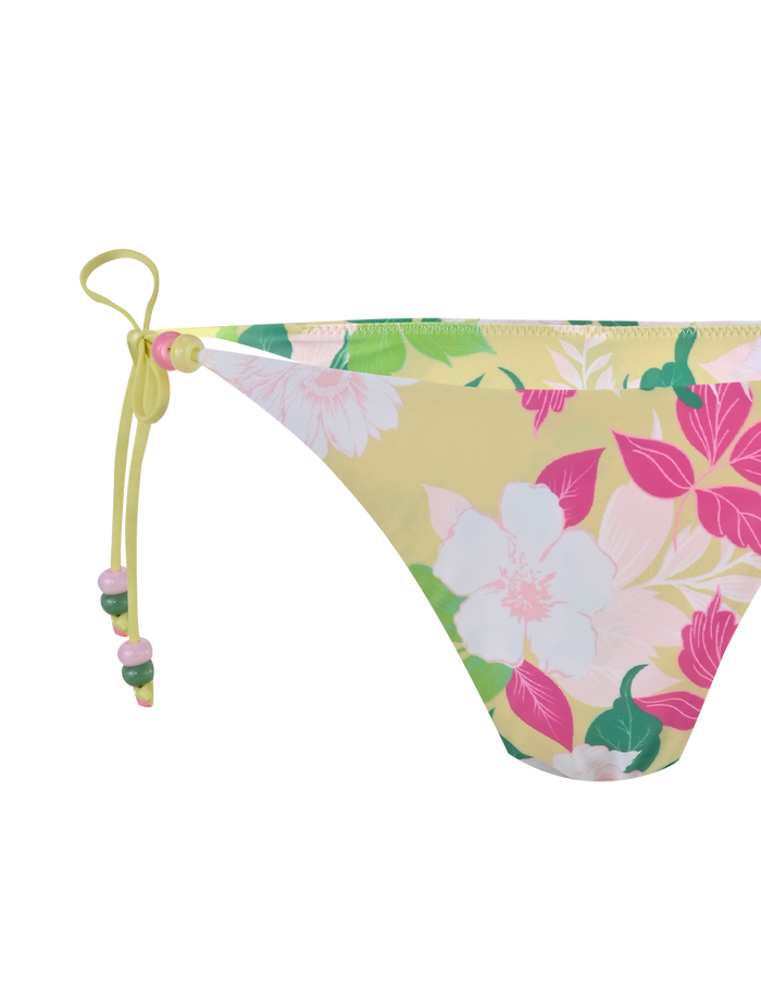 A close-up of the TIGERMIST FINLEA BIKINI BOTTOM - PAISLEY BORDER featuring a yellow floral print, cheeky cut, side tie with bow, and beaded accents.