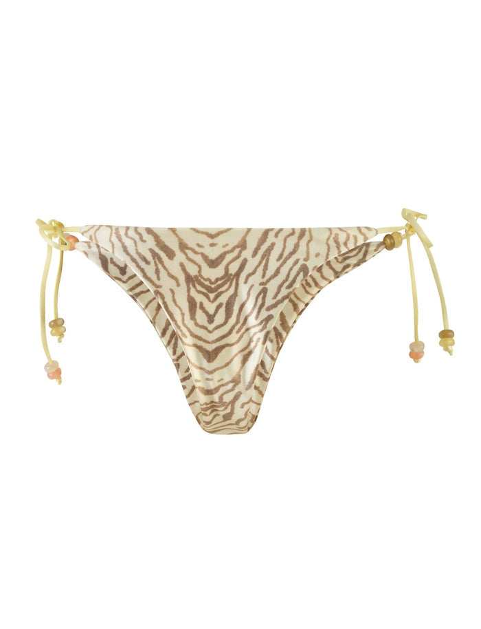 The FINLEA BIKINI BOTTOM - YELLOW : ZEBRA by TIGERMIST is a pair of bikini bottoms with a cheeky bikini cut and a yellow zebra print pattern in beige and brown tones. The swimsuit features high stretch fabric for comfort, along with yellow string ties on both sides, each adorned with small decorative beads.