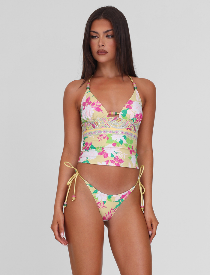 A woman with long dark hair and a neutral expression stands against a plain background, wearing the TIGERMIST FINLEA TANKINI TOP - PAISLEY BORDER. She looks slightly to the side.