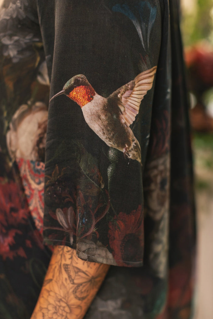 Model wearing the Flight of Fancy Artist Dress featuring vintage floral paintings and a bouquet of hummingbirds symbolizing hope and joy – Market of Stars.