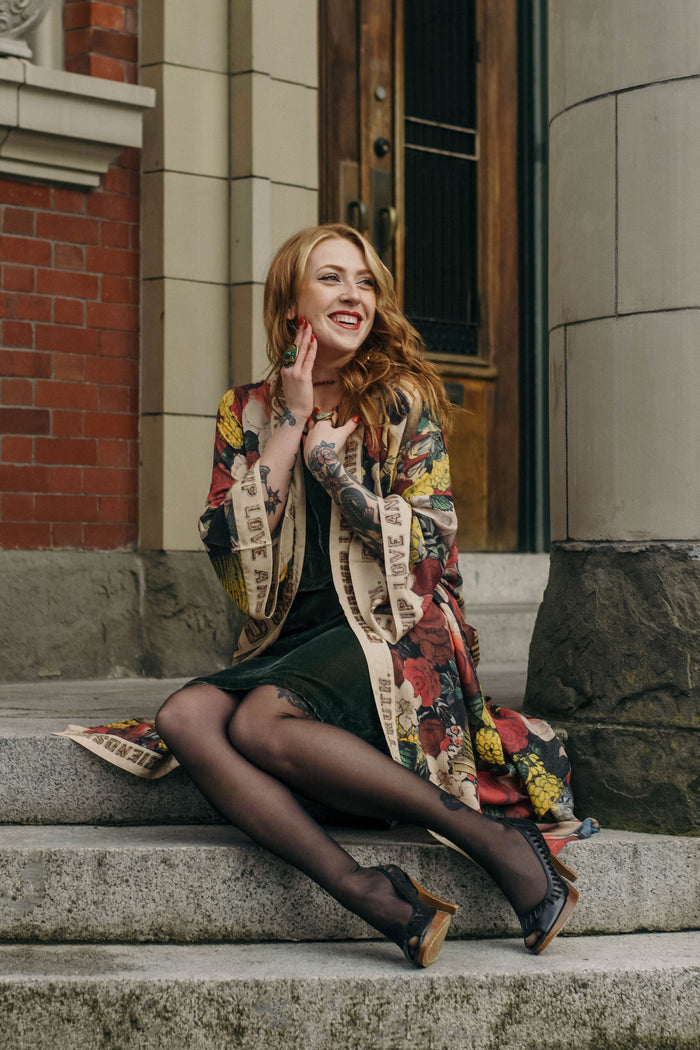 Model wearing our long, eclectic opera duster featuring vintage symbols of love, kindness, and truth in a bold archive-inspired print with removable belt – Market of Stars.