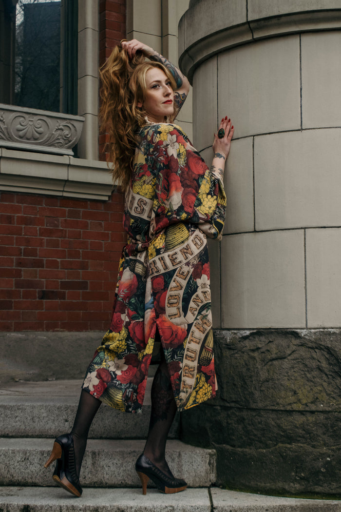 Model wearing our long, eclectic opera duster featuring vintage symbols of love, kindness, and truth in a bold archive-inspired print with removable belt – Market of Stars.