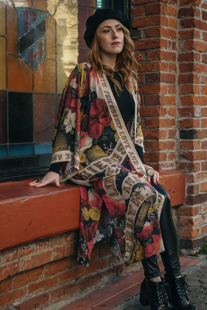 Model wearing our long, eclectic opera duster featuring vintage symbols of love, kindness, and truth in a bold archive-inspired print with removable belt – Market of Stars.