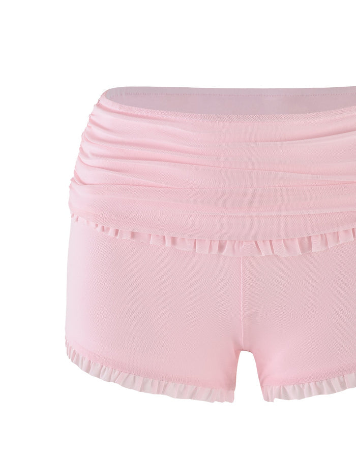 The GINNY SHORT - PINK : BABY PINK by TIGERMIST is a pair of baby pink ballet shorts with a ruched waistband and ruffled trim at both the waistline and leg openings, providing a delicate, feminine look. The high-stretch fabric ensures comfort and flexibility, making it perfect for dance or athletic activities.