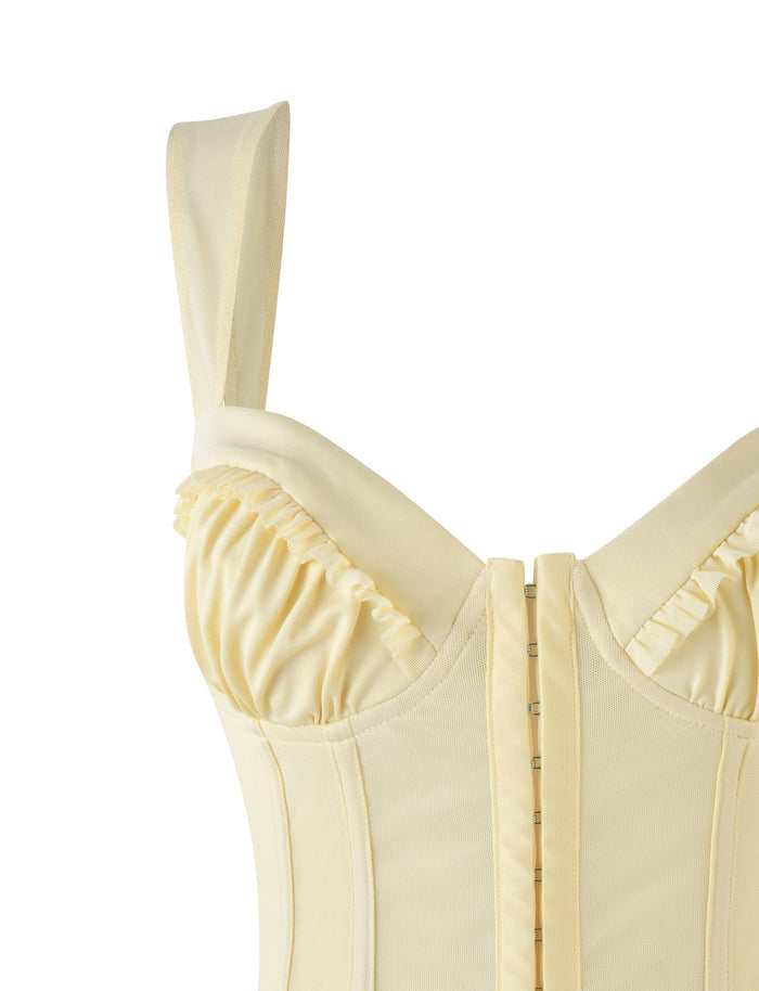 Close-up of the light yellow GINNY TOP - YELLOW : LEMON by TIGERMIST, showcasing its sweetheart neckline with structured cups and ruffled detailing on the bust. It includes vertical boning and a row of hooks for closure. The smooth fabric enhances the bodycon silhouette, with one strap visible on the side.