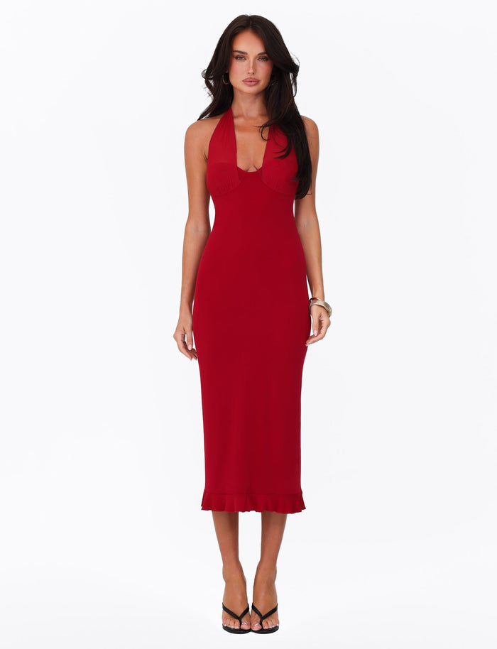 A person with long dark hair wears the sleeveless, fitted Granger Midi Dress in Cherry Red by Tigermist, featuring a ruffled hem, paired with black heels and standing against a plain white background.
