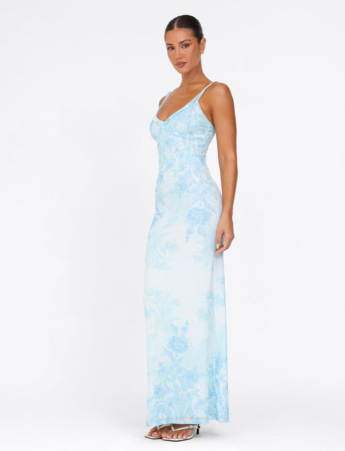 A woman gracefully poses in the TIGERMIST GUILIANNA FRILL MAXI DRESS - BLUE : FLORAL : TAPESTRY against a plain white background. This dress, made from high stretch fabric, showcases adjustable frill shoulder straps as she looks toward the camera, one leg slightly forward to highlight its elegant fit.