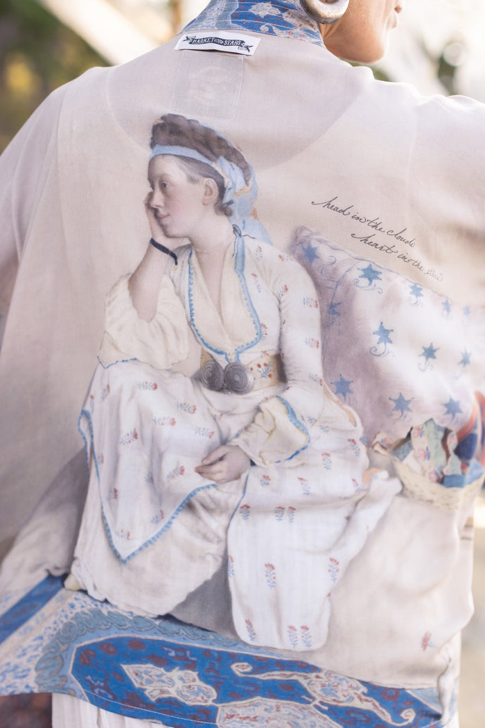 Model wearing the Head in the Clouds Opera Duster featuring Liotard’s portrait of his wife with Turkish textiles, starry sleeves, and poetic script – Market of Stars.