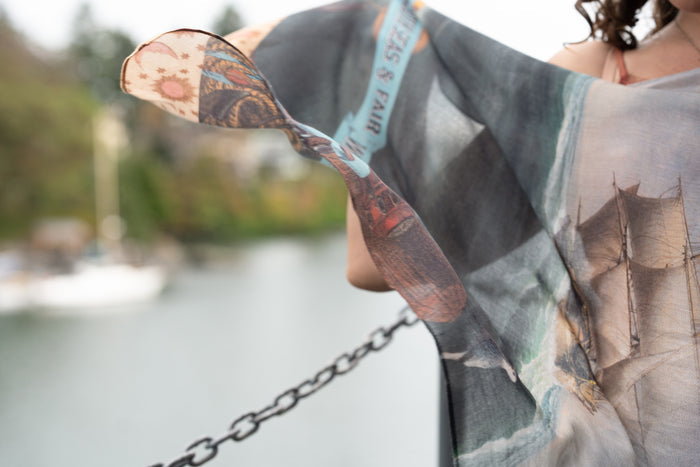 Model wearing the Hold Fast bamboo viscose scarf featuring a Victorian woman bravely rowing through a storm, seagulls, and rainbow horizon – Market of Stars.