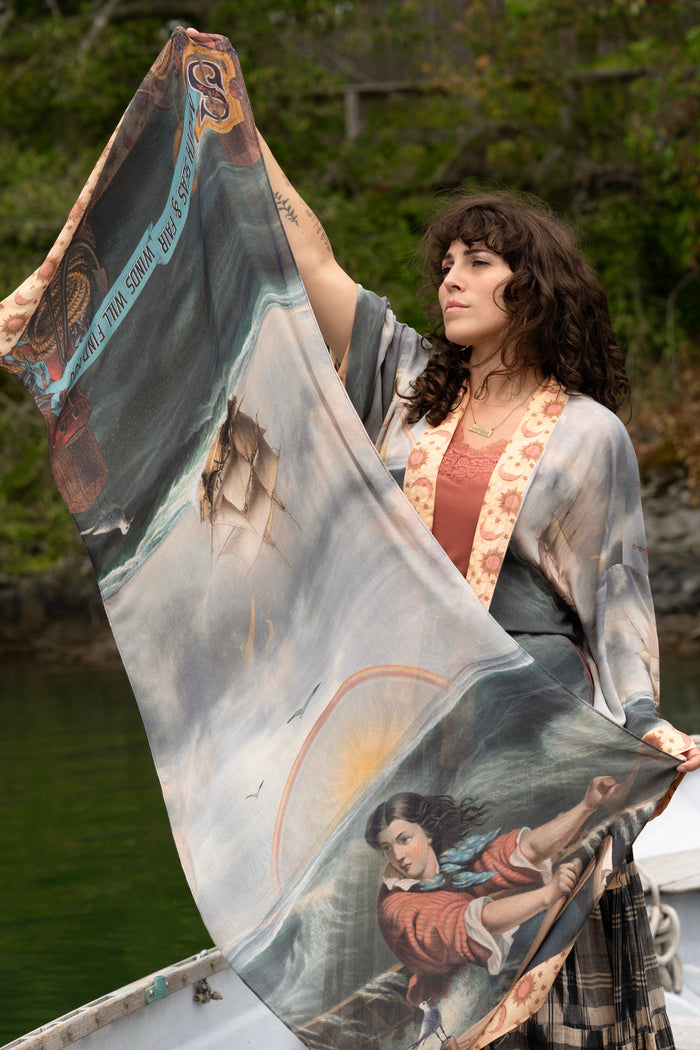 Model wearing the Hold Fast bamboo viscose scarf featuring a Victorian woman bravely rowing through a storm, seagulls, and rainbow horizon – Market of Stars.