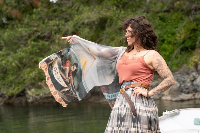 Model wearing the Hold Fast bamboo viscose scarf featuring a Victorian woman bravely rowing through a storm, seagulls, and rainbow horizon – Market of Stars.