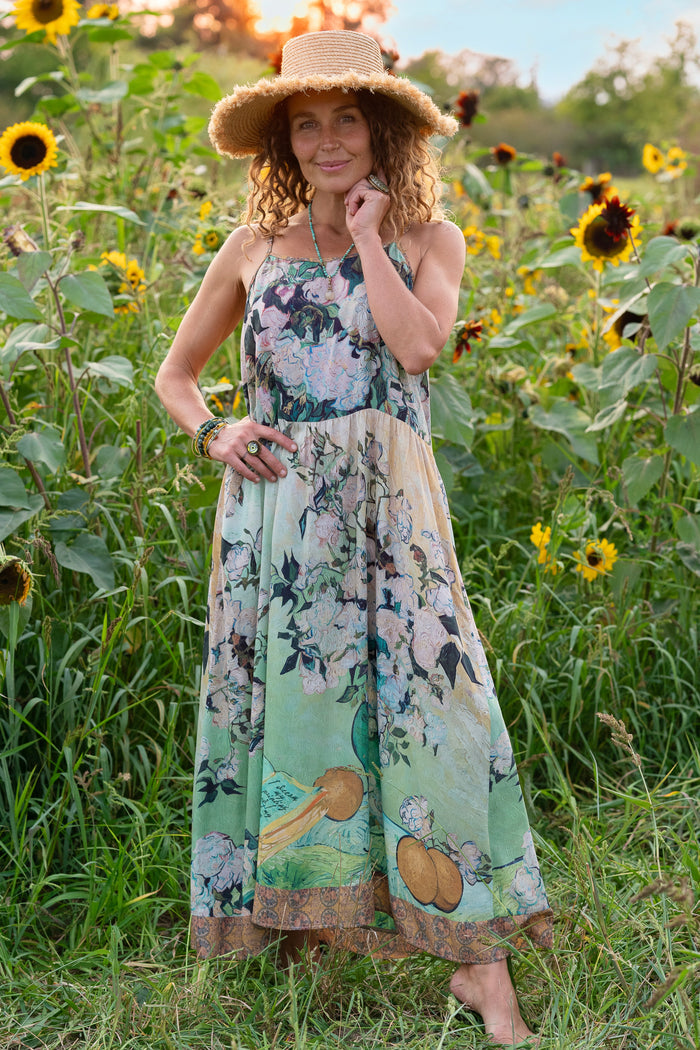 Model wearing bamboo viscose slip dress featuring Van Gogh artwork and quote, with painted blossoms, book, sun, and eye in rich sunny tones of jade and gold - Market of Stars