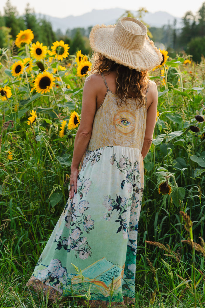 Model wearing bamboo viscose slip dress featuring Van Gogh artwork and quote, with painted blossoms, book, sun, and eye in rich sunny tones of jade and gold - Market of Stars