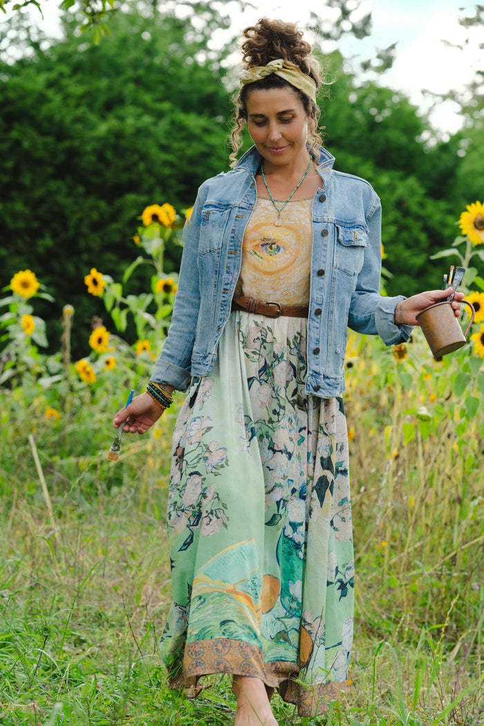 Model wearing bamboo viscose slip dress featuring Van Gogh artwork and quote, with painted blossoms, book, sun, and eye in rich sunny tones of jade and gold - Market of Stars