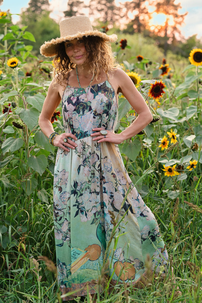 Model wearing bamboo viscose slip dress featuring Van Gogh artwork and quote, with painted blossoms, book, sun, and eye in rich sunny tones of jade and gold - Market of Stars