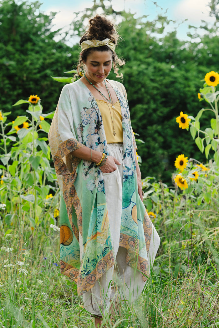 Model wearing mid-length duster featuring Van Gogh artwork and quote, with painted blossoms, book, sun, and eye in rich tones of jade and gold - Market of Stars