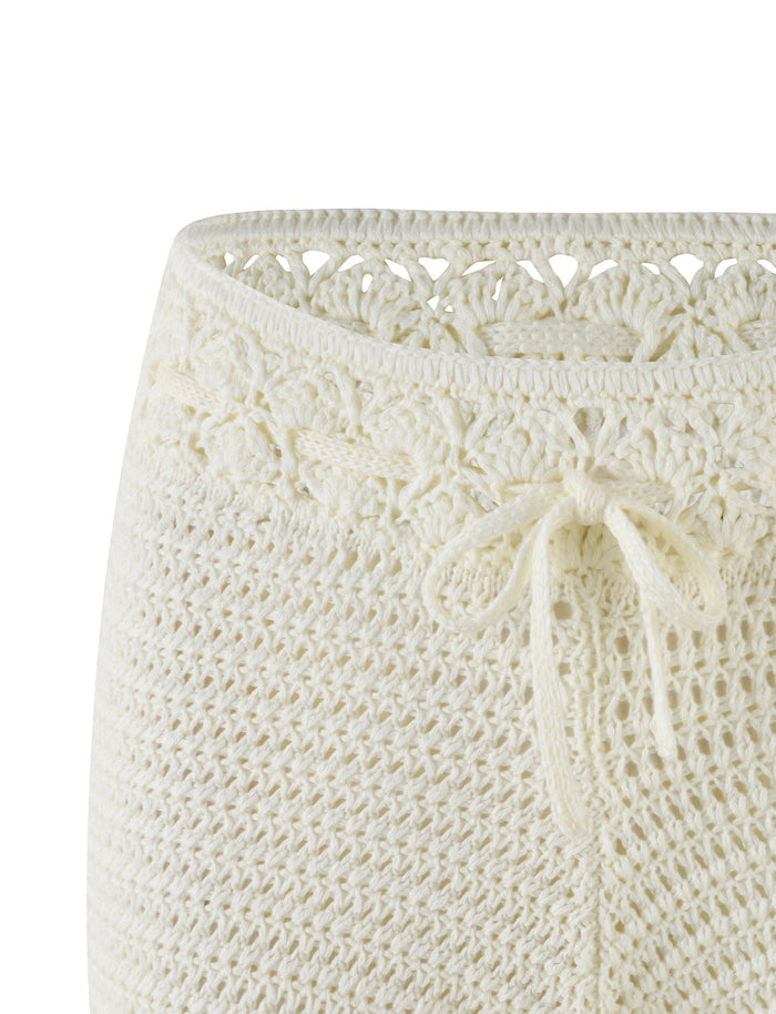 Close-up of the JONAS SHORT - WHITE : CREAM by TIGERMIST, showcasing the upper portion. The intricate knitted pattern features a decorative lace design near the waistband and a delicate drawstring tied in a bow at the front. The super mini length crochet work is detailed and textured, with contrast stitch accents.