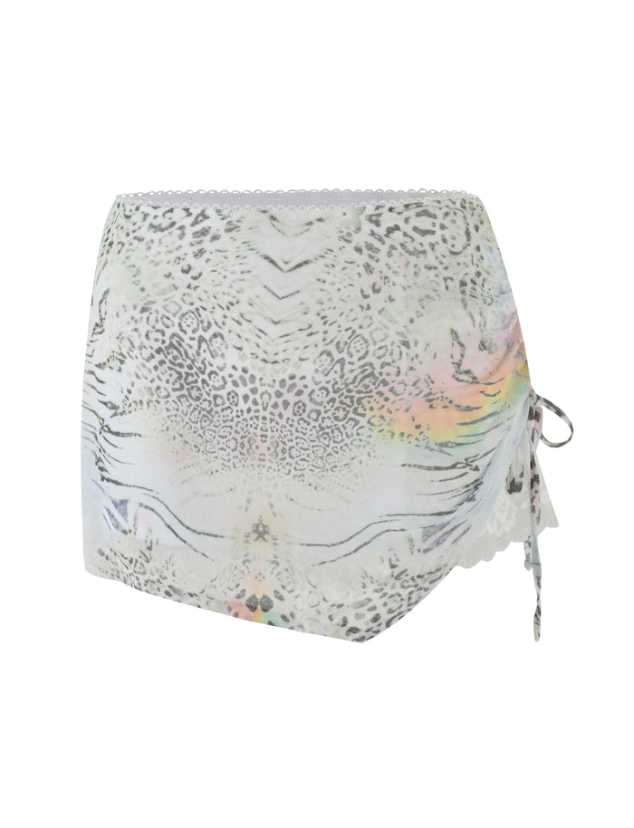 The JOSEPHINE MINI SKIRT by TIGERMIST features a white animal print design with light grey leopard spots, lace trim on both edges, and a side tie detail accented with subtle pastel rainbow hues.