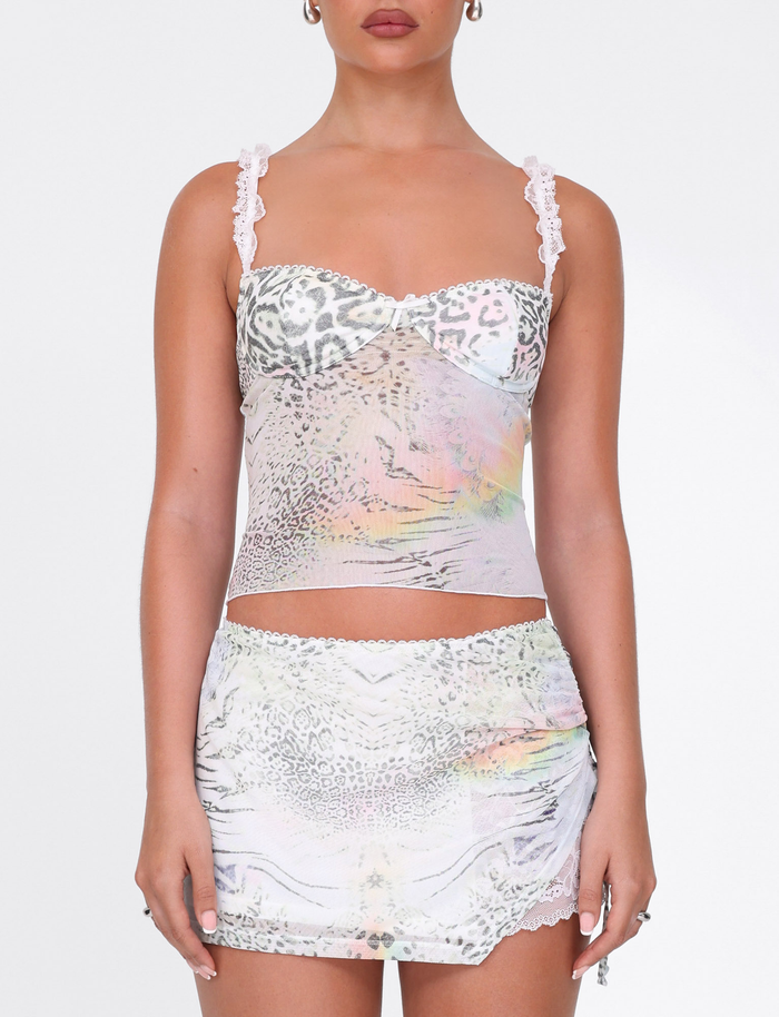A woman in the TIGERMIST JOSEPHINE TOP - WHITE : ANIMAL PRINT, a fitted camisole with lace straps, and matching mini skirt stands facing forward against a plain white background.