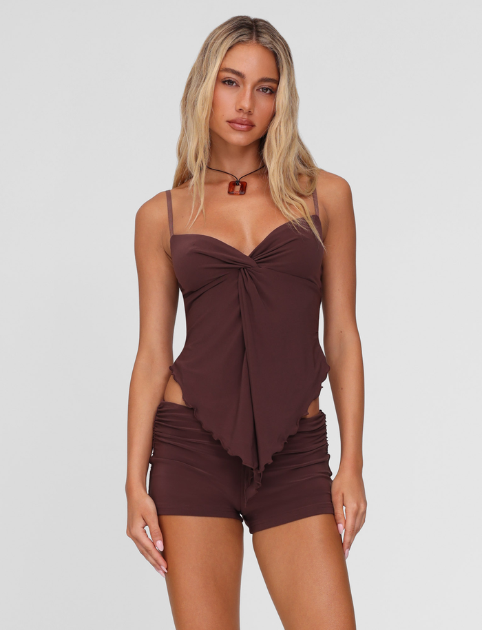 A woman with long blonde hair models the TIGERMIST JOVIENNE TOP - BROWN : CHOCOLATE and matching shorts, standing against a plain light gray background and looking at the camera with a neutral expression.