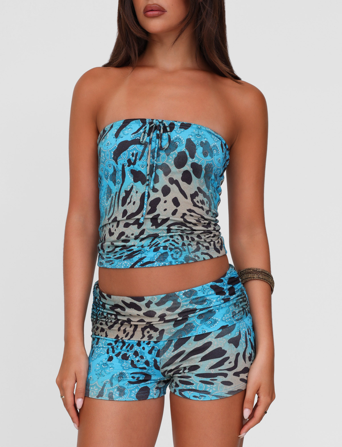 A woman models TIGERMIST’s KARINA SHORT - MULTI: LEOPARD SWIRL, a blue and gray animal print strapless top with matching high-stretch blue leopard mini shorts, standing against a plain white background.