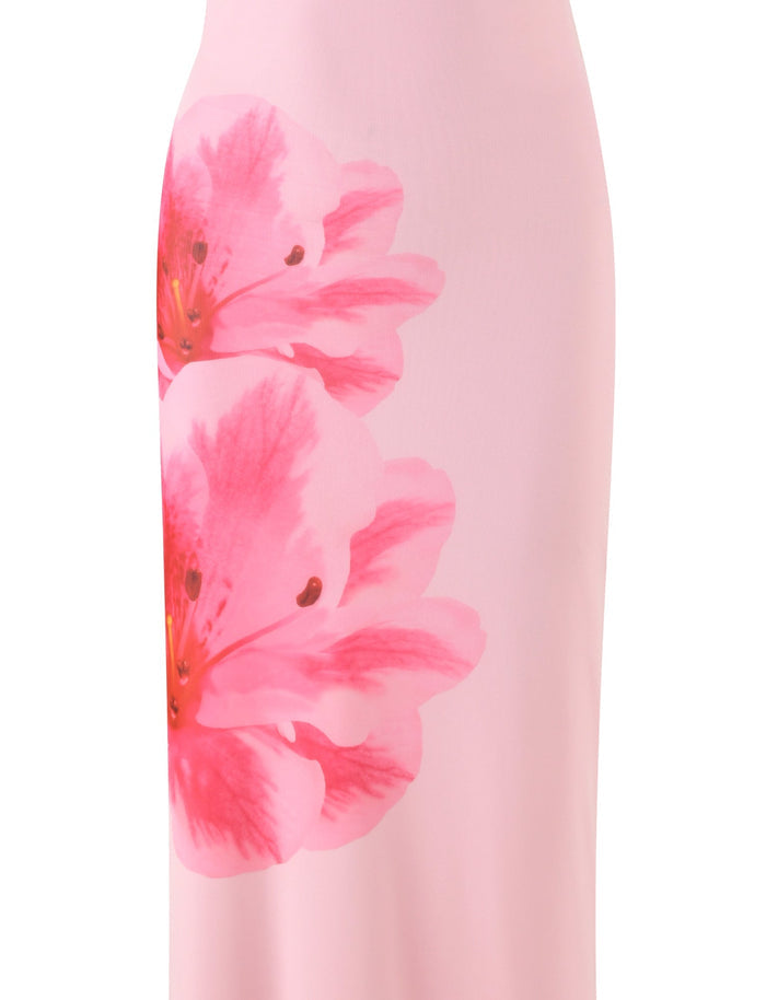 Close-up of the KARTER DRESS - PINK : BABY PINK from TIGERMIST, featuring a smooth light pink fabric adorned with a large, vibrant print of two pink flowers with reddish centers. The material appears smooth and suggests that this piece is part of a maxi length dress.