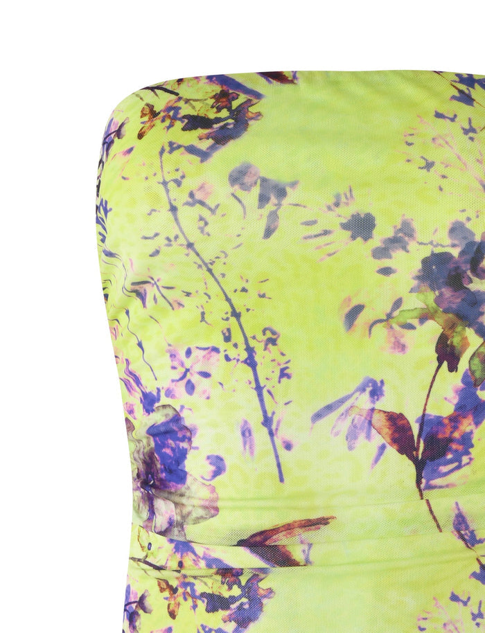 A close-up of the KELLAN TOP - GREEN by TIGERMIST against a bright yellow background, showcasing a vibrant and summery floral pattern with abstract motifs in shades of purple, pink, and green.