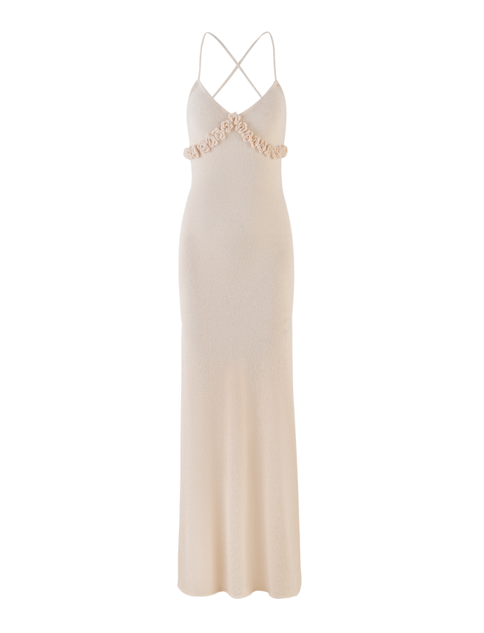 The TIGERMIST LAVELLE MAXI DRESS in Cream is a floor-length, sleeveless knit dress with thin criss cross straps, v-neckline, floral embellishments at the bust, open back, fitted bodice, and gently flared skirt for an elegant look.