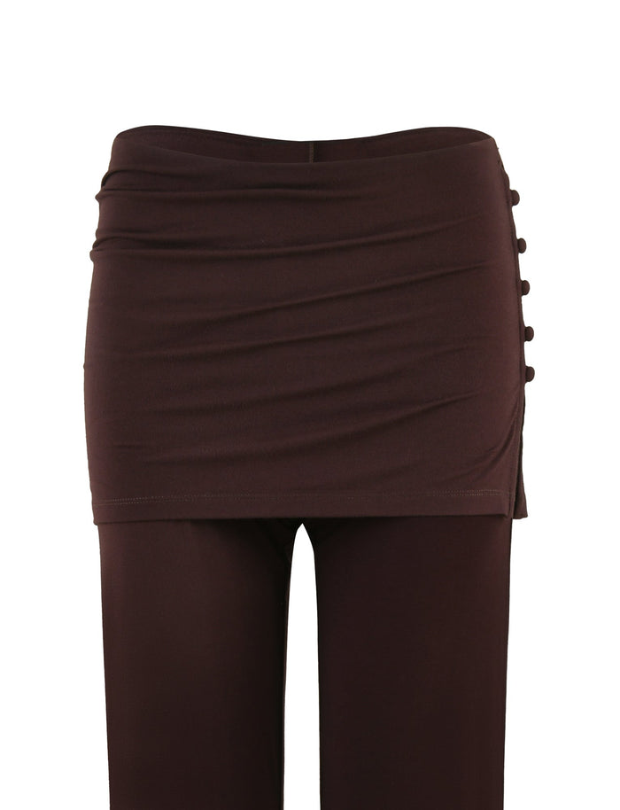 The LEILANI PANT - BROWN : CHOCOLATE by TIGERMIST is a stylish pair of pants featuring a flared leg and an attached wraparound skirt at the waist with side button detailing on the right. The high-stretch fabric of the ruched-texture skirt adds a fashionable touch to the design.