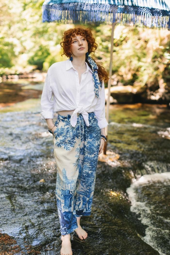 Model wearing Let the Light In linen Artist Pant featuring print of Delft blue and white landscape pottery, and positive message of light and hope - Market of Stars
