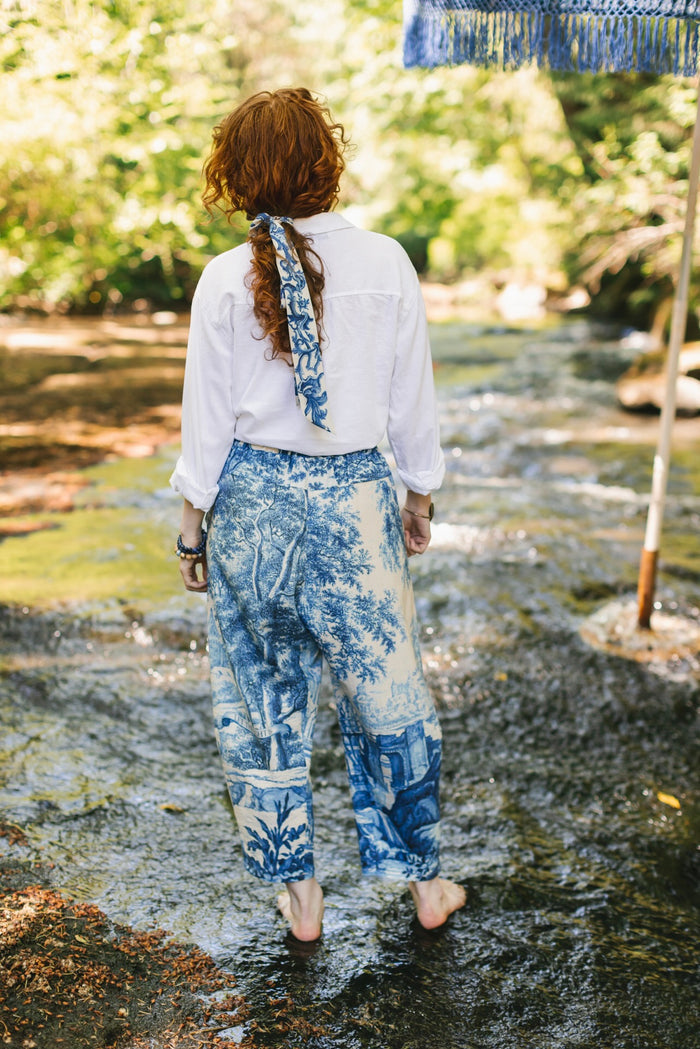 Model wearing Let the Light In linen Artist Pant featuring print of Delft blue and white landscape pottery, and positive message of light and hope - Market of Stars