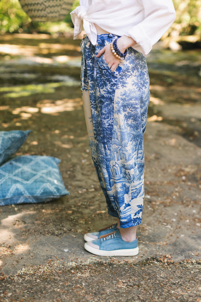 Model wearing Let the Light In linen Artist Pant featuring print of Delft blue and white landscape pottery, and positive message of light and hope - Market of Stars