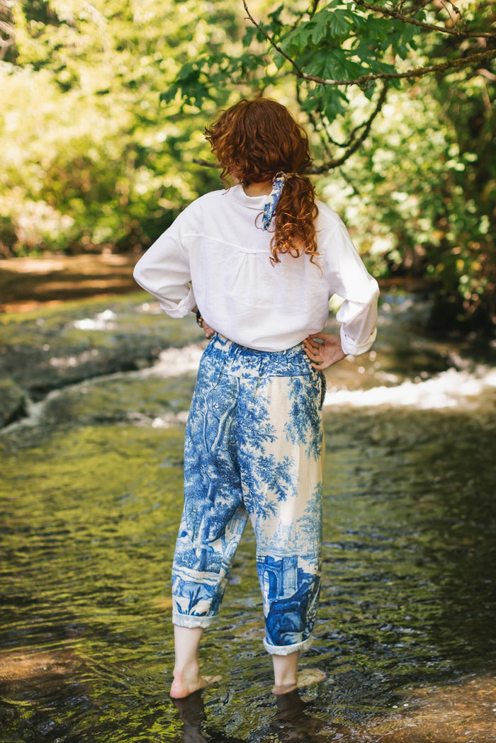 Model wearing Let the Light In linen Artist Pant featuring print of Delft blue and white landscape pottery, and positive message of light and hope - Market of Stars