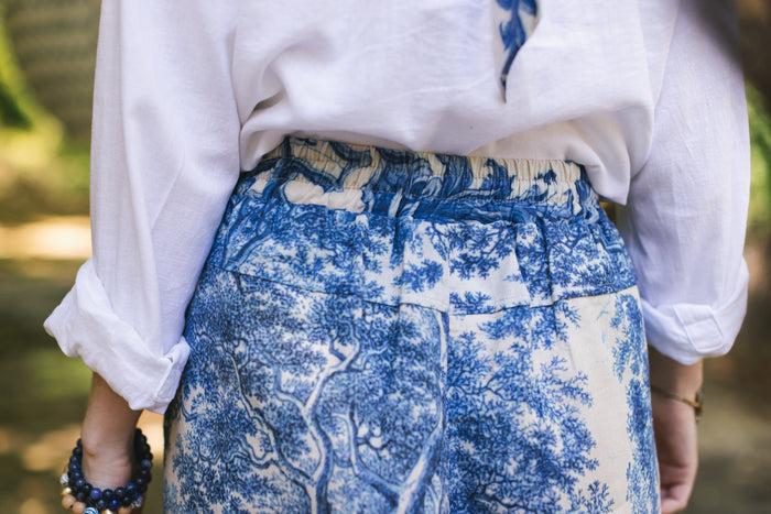 Model wearing Let the Light In linen Artist Pant featuring print of Delft blue and white landscape pottery, and positive message of light and hope - Market of Stars