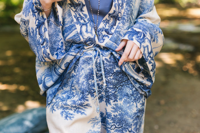 Model wearing Let the Light In linen Artist Pant featuring print of Delft blue and white landscape pottery, and positive message of light and hope - Market of Stars