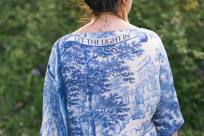 Model wearing Let the Light In bamboo viscose Luxe Tee shirt featuring print of Delft blue and white landscape pottery, and positive message of light and hope - Market of Stars