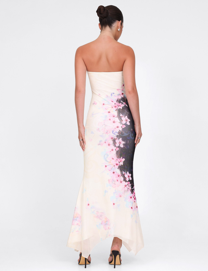A woman with her hair in a bun models the TIGERMIST LILLIAN MAXI DRESS - MULTI: FLORAL: CHERRY BLOSSOM, showing its high-stretch strapless mesh design as she faces away in nude heels against a white background.