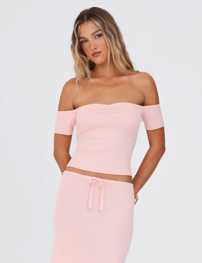 A woman with long blond hair is wearing the LILYANNA TOP in baby pink by TIGERMIST, along with a matching skirt, both crafted from stretchy fabric. She stands against a plain white background with her arms by her sides, looking directly at the camera.