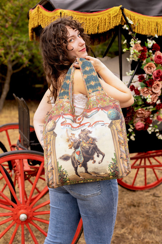 Model carrying a linen tote bag ft. a woman astride a rearing horse, soft vintage florals, rosettes and lithographs from the 1800's - Market of Stars