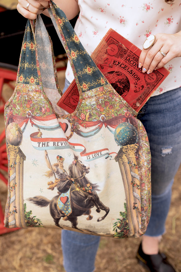 Model carrying a linen tote bag ft. a woman astride a rearing horse, soft vintage florals, rosettes and lithographs from the 1800's - Market of Stars