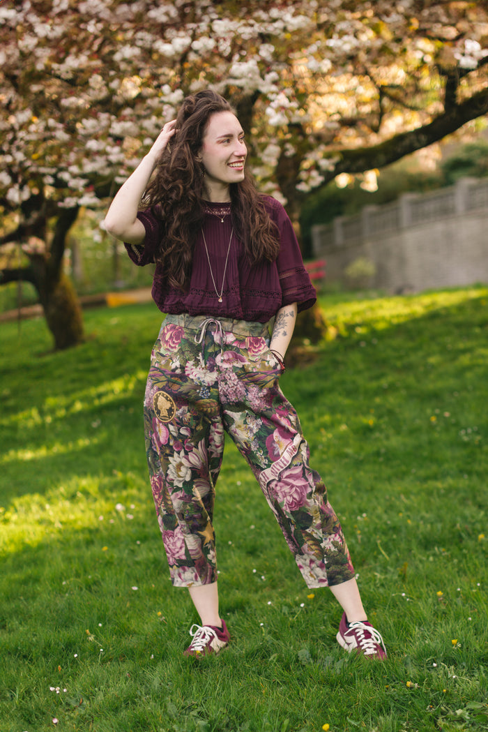 Model wearing linen blend artist pants featuring antique wishbone–Victorian coin–evening star–dandelion art and “Wish with Me” banner on floral background – Market of Stars