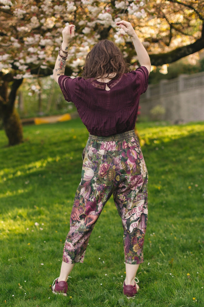 Model wearing linen blend artist pants featuring antique wishbone–Victorian coin–evening star–dandelion art and “Wish with Me” banner on floral background – Market of Stars