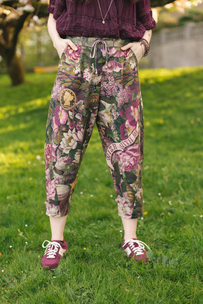 Model wearing linen blend artist pants featuring antique wishbone–Victorian coin–evening star–dandelion art and “Wish with Me” banner on floral background – Market of Stars