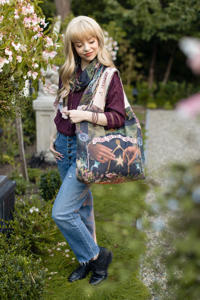 Model holding linen blend market tote featuring Victorian wishbone–vintage coin–evening star–dandelion–and “Best Wishes” banner on floral background – Market of Stars