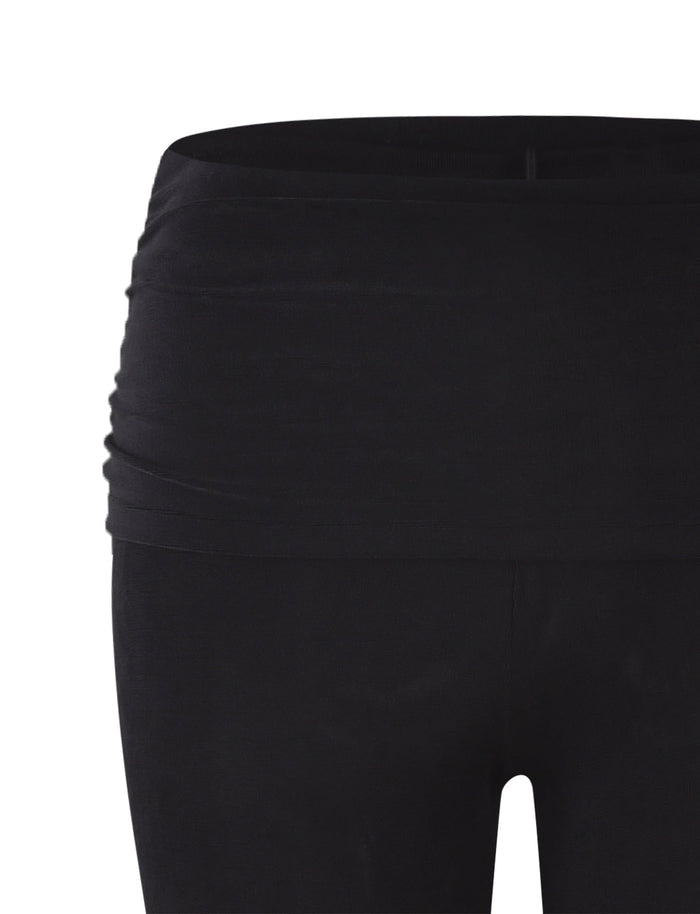 A close-up of the upper part of the MAKENA PANT - BLACK from TIGERMIST features a wide waistband, with smooth fabric that is slightly ruched on the side, ensuring a snug and comfortable fit. The white background highlights the black color and texture of these yoga pants or leggings.