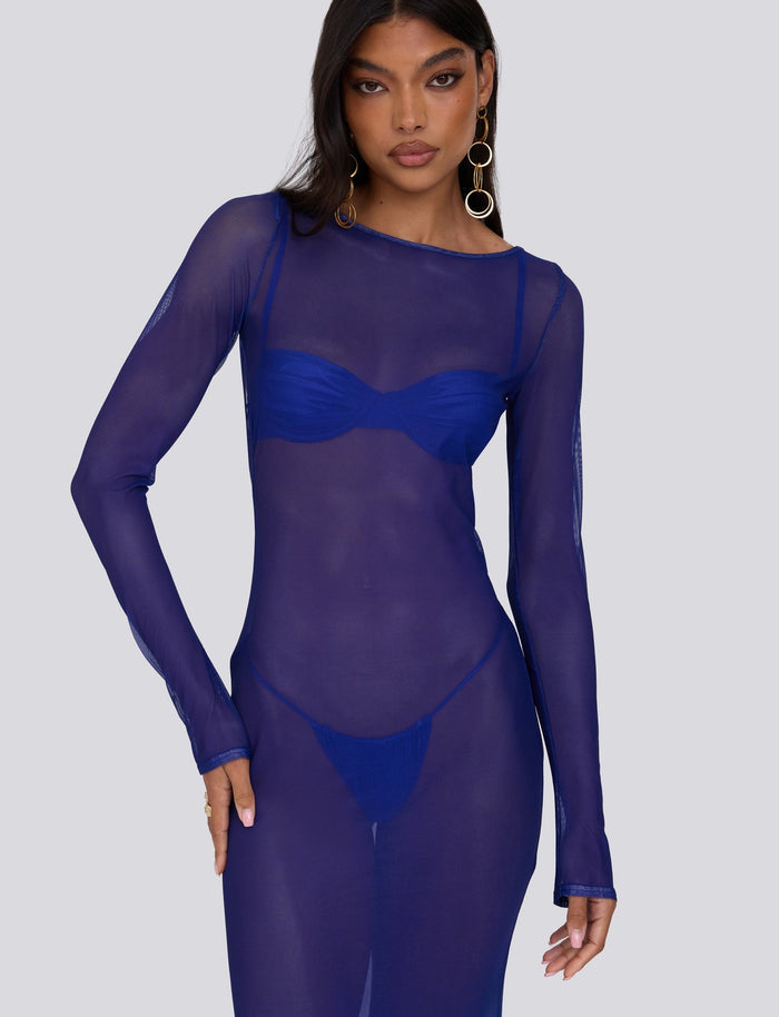 A woman with long dark hair wears the MEILANI DRESS - BLUE : OMBRE from TIGERMIST over a matching blue bra and panties. She accessorizes with large gold hoop earrings and poses against a plain light gray background.